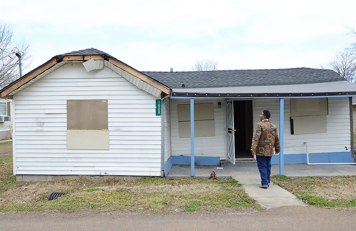 A man stands in front of a boarded up house.