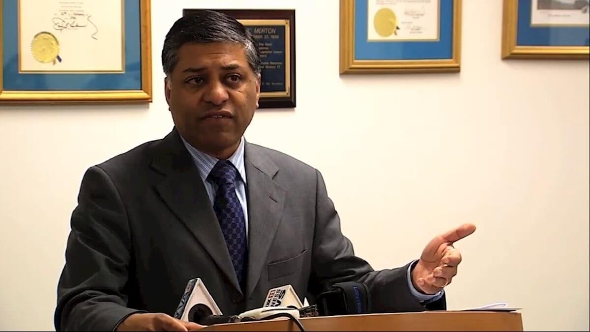 Dr. Rahul Gupta stands at a podium that has television microphones on top of it.