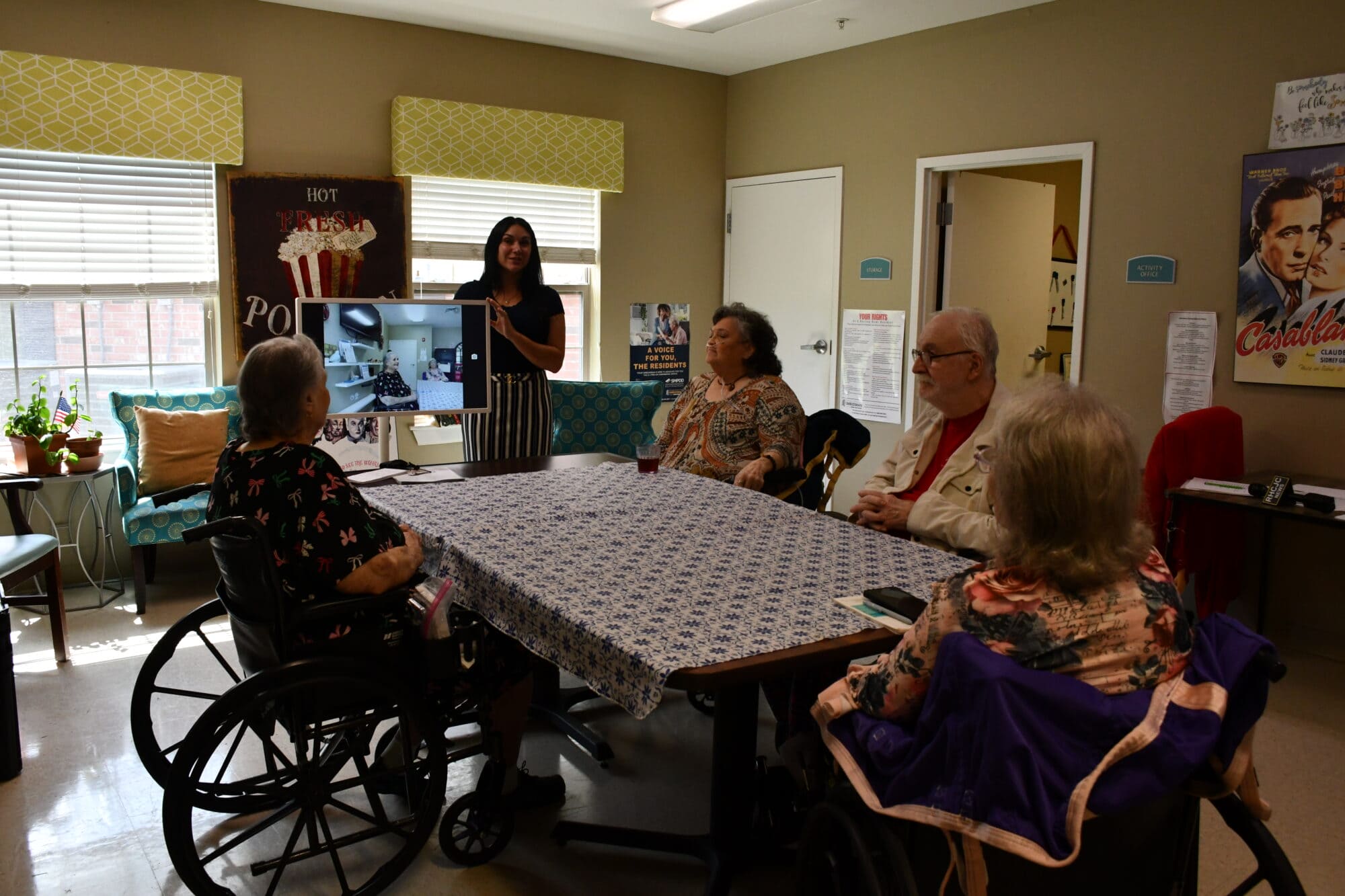 Four residents sit around a table as a woman standing in front of them explains video conferencing.