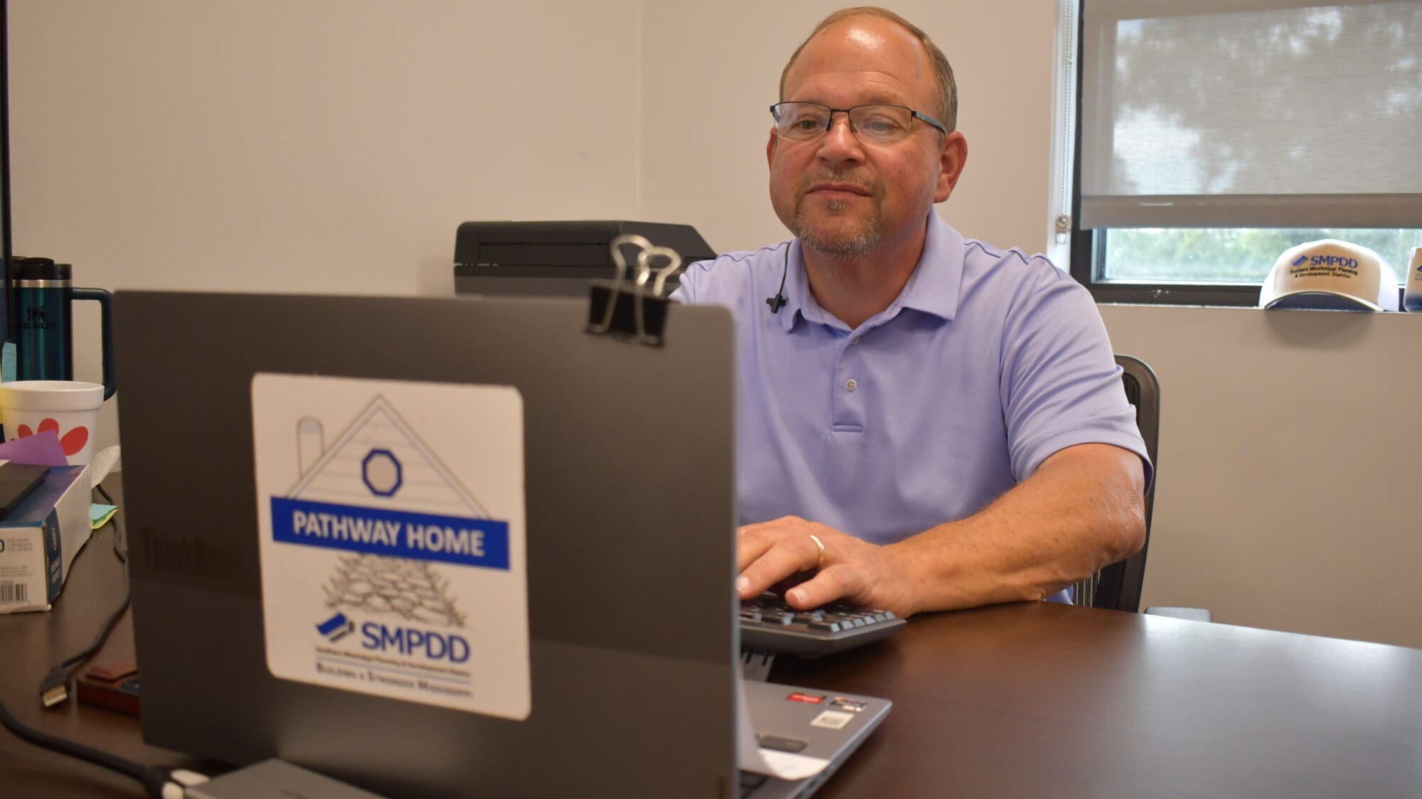 Chris Nixon sits behind a desk with a laptop in the foreground displaying a label that reads “Pathway Home SMPDD."